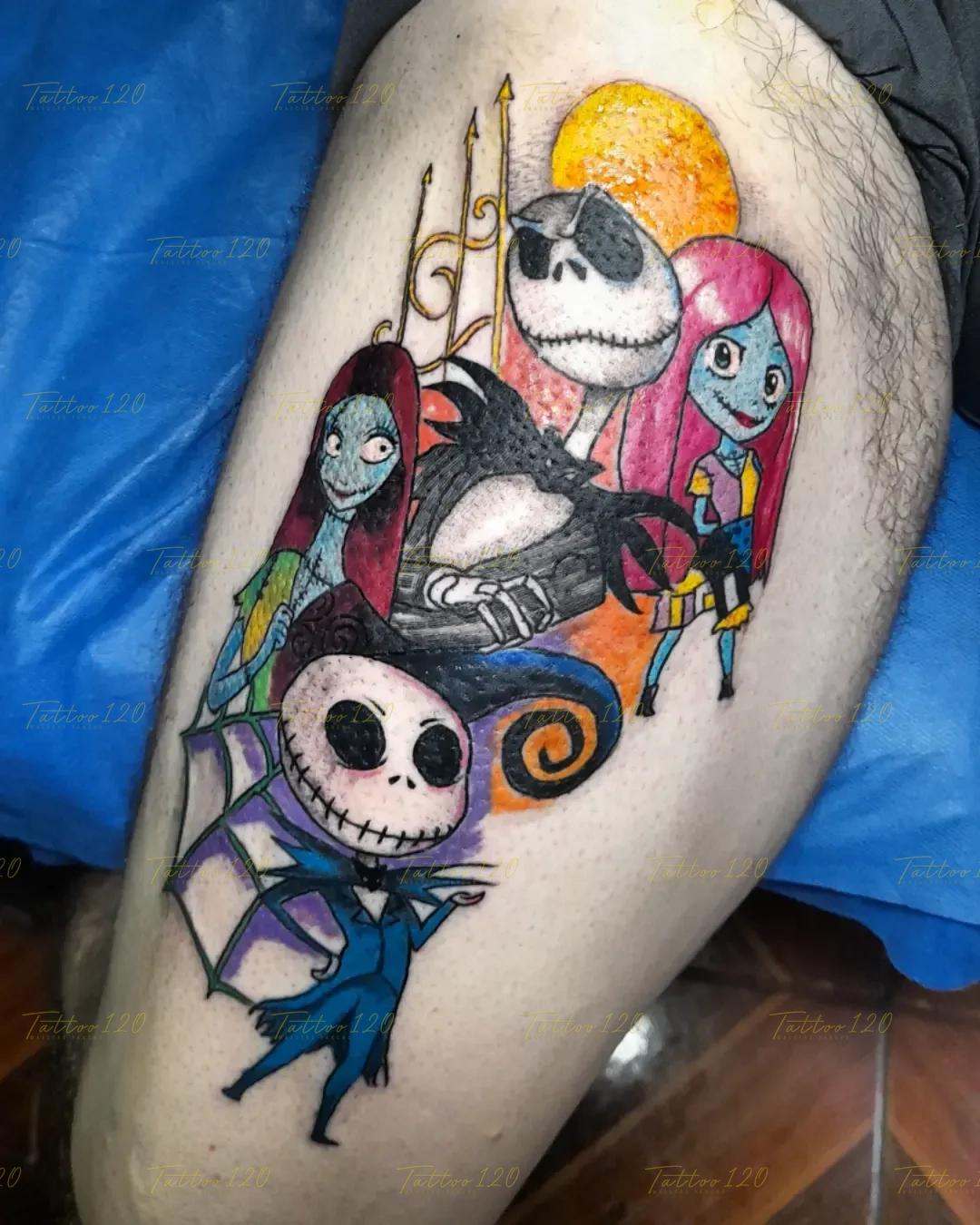 Tatuaje grande a color en el muslo con varios personajes de El extraño mundo de Jack, incluyendo a Jack Skellington, Sally y la alcaldesa, bajo una luna llena naranja. estilo anime, manga e ilustraciones, realizado en el estudio Tattoo120 en Colina, Región Metropolitana.