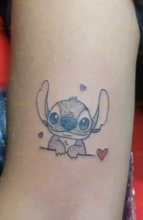 Tatuaje pequeño y minimalista del personaje Stitch de Disney asomándose sobre una línea, delineado en negro con pequeños corazones rojos a los lados. estilo anime, manga e ilustraciones, realizado en el estudio Tattoo120 en Colina, Región Metropolitana.