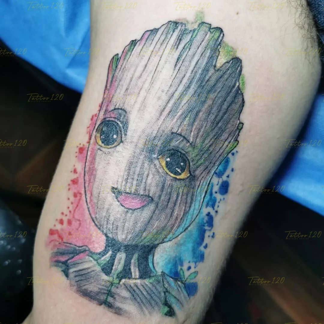 Tatuaje a color del personaje Baby Groot de Guardianes de la Galaxia sonriendo, con un fondo de salpicaduras de acuarela en tonos rosa y azul. estilo anime, manga e ilustraciones, realizado en el estudio Tattoo120 en Colina, Región Metropolitana.