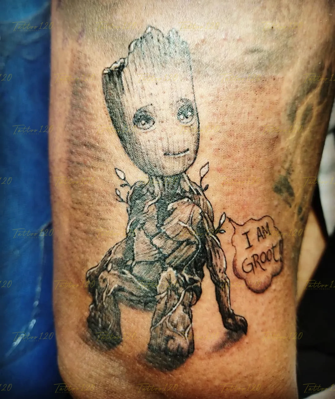Tatuaje en blanco y negro de Baby Groot de Guardianes de la Galaxia sentado, con un bocadillo de diálogo estilo cómic que dice 'I AM GROOT!'. estilo anime, manga e ilustraciones, realizado en el estudio Tattoo120 en Colina, Región Metropolitana.