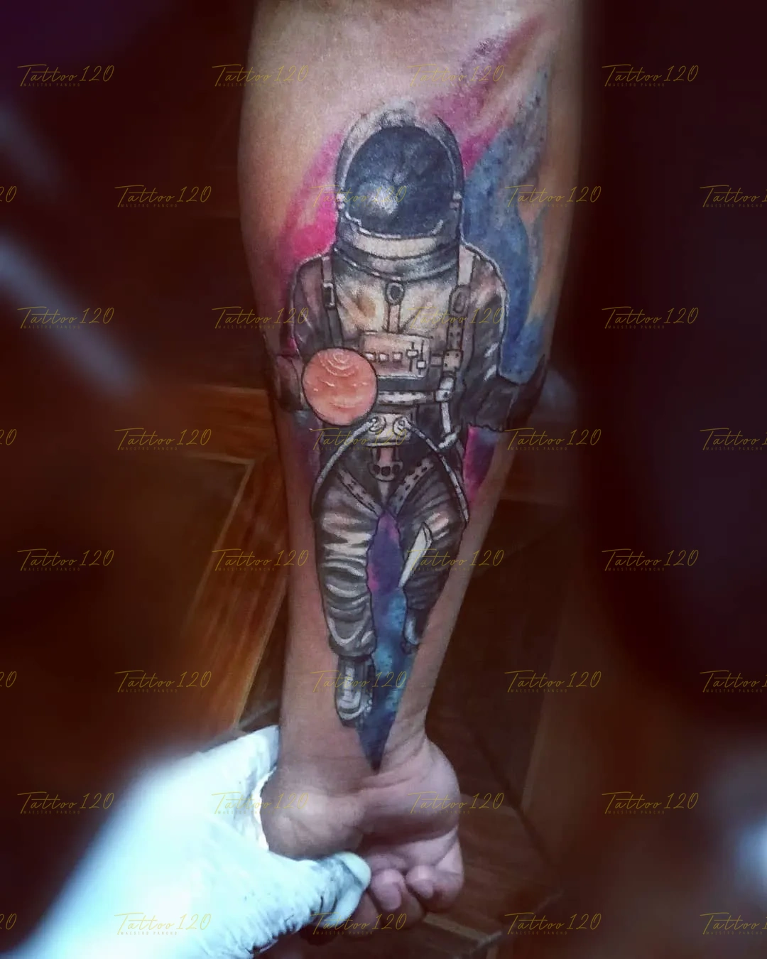 Tatuaje detallado en el antebrazo de un astronauta de cuerpo entero flotando en el espacio, rodeado por un fondo de nebulosa cósmica en tonos rosa y azul. estilo anime, manga e ilustraciones, realizado en el estudio Tattoo120 en Colina, Región Metropolitana.