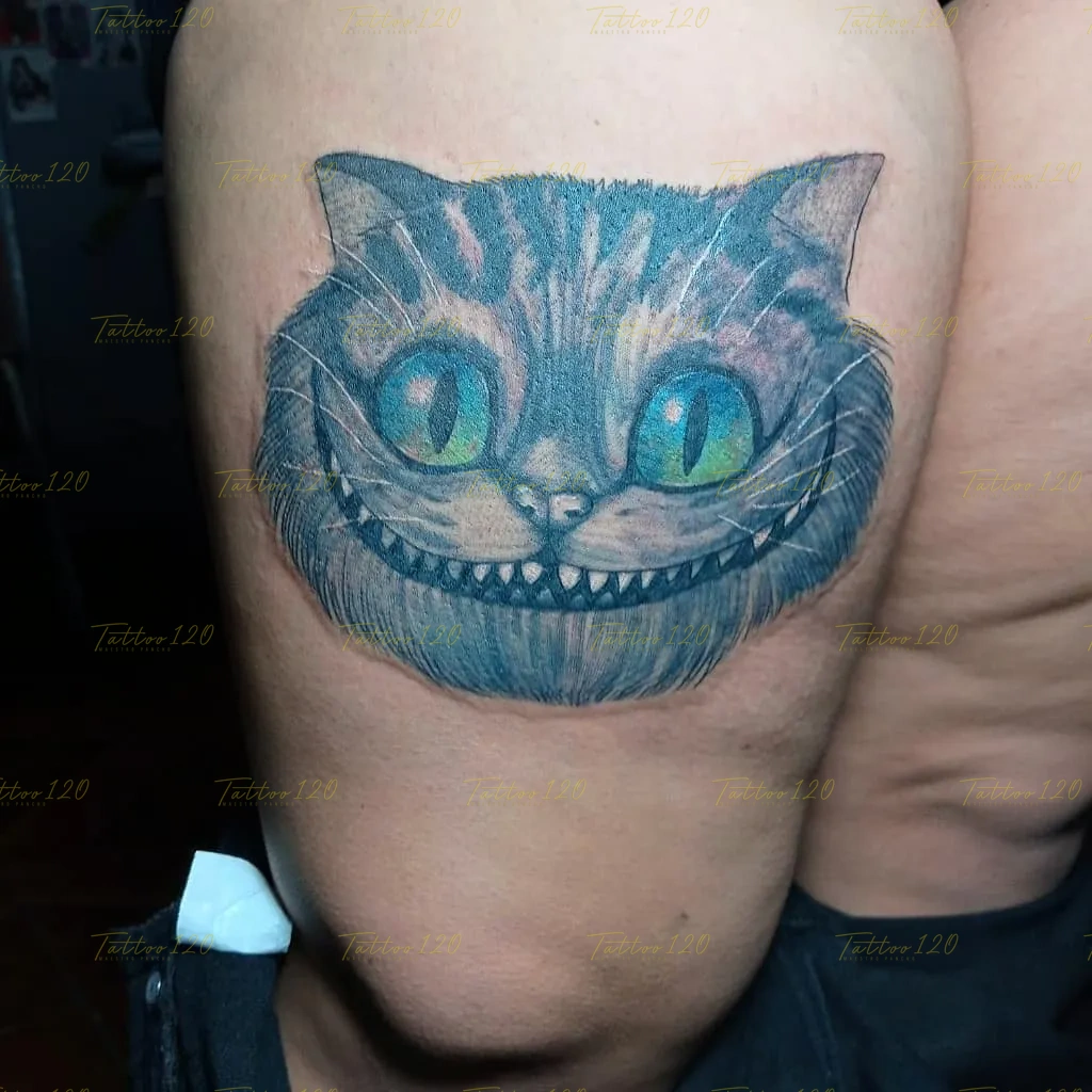 Tatuaje a color en el muslo con el rostro del Gato de Cheshire de Alicia en el País de las Maravillas resaltando sus grandes ojos celestes, estilo anime, manga e ilustraciones, realizado en el estudio Tattoo120 en Colina, Región Metropolitana.