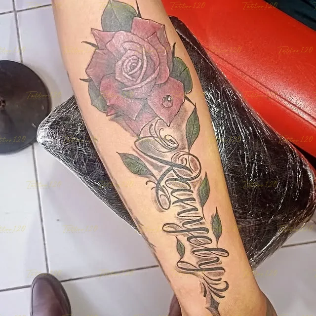 Tatuaje del nombre Ranyelby en tipografía cursiva fluida junto a una gran rosa sombreada en el antebrazo, en estilo de letras, frases y chicano, realizado en el estudio Tattoo120 en Colina, Región Metropolitana.