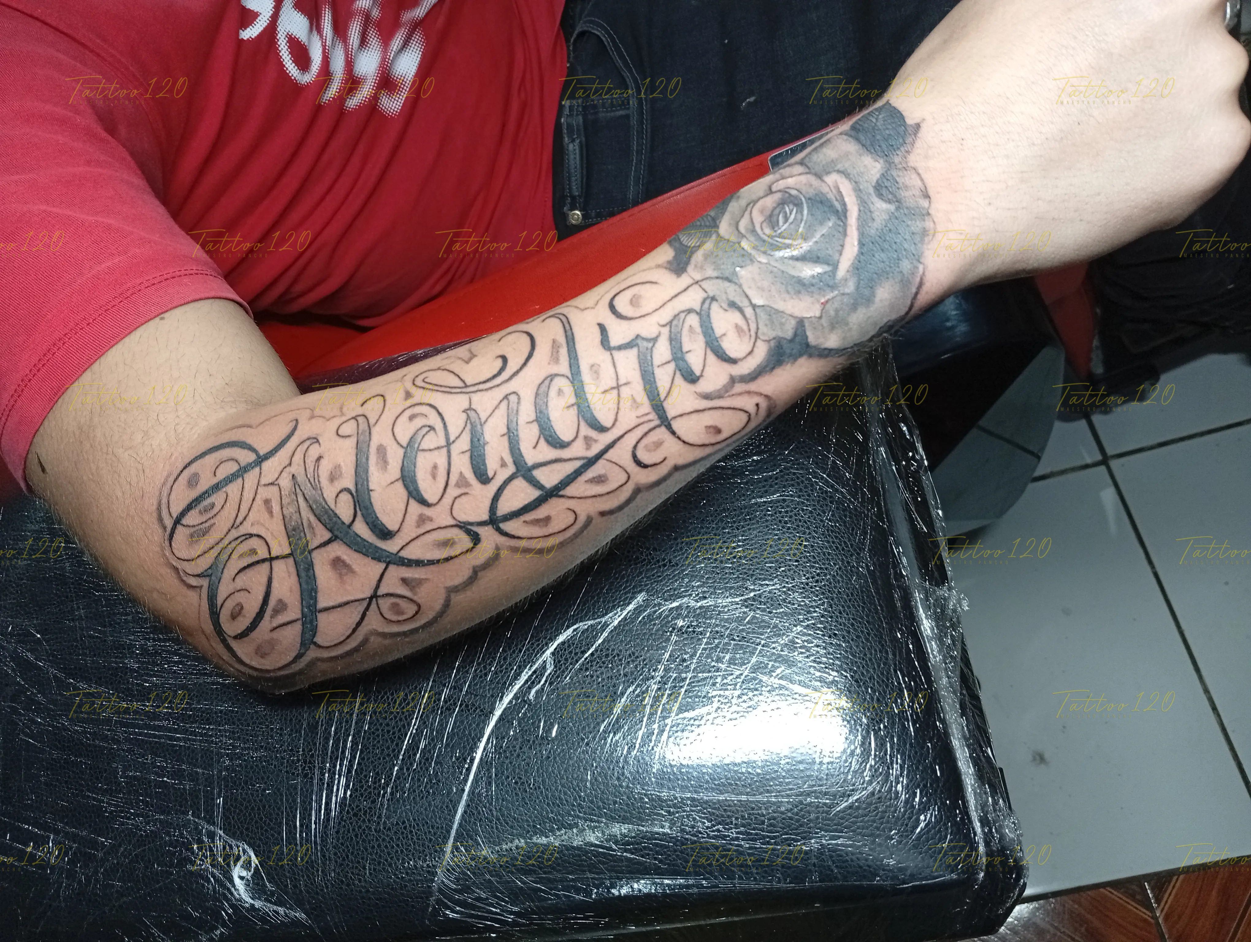 Tatuaje del nombre Alondra realizado con letras cursivas de estilo script chicano y una rosa detallada en tinta negra, en estilo de letras, frases y chicano, realizado en el estudio Tattoo120 en Colina, Región Metropolitana.
