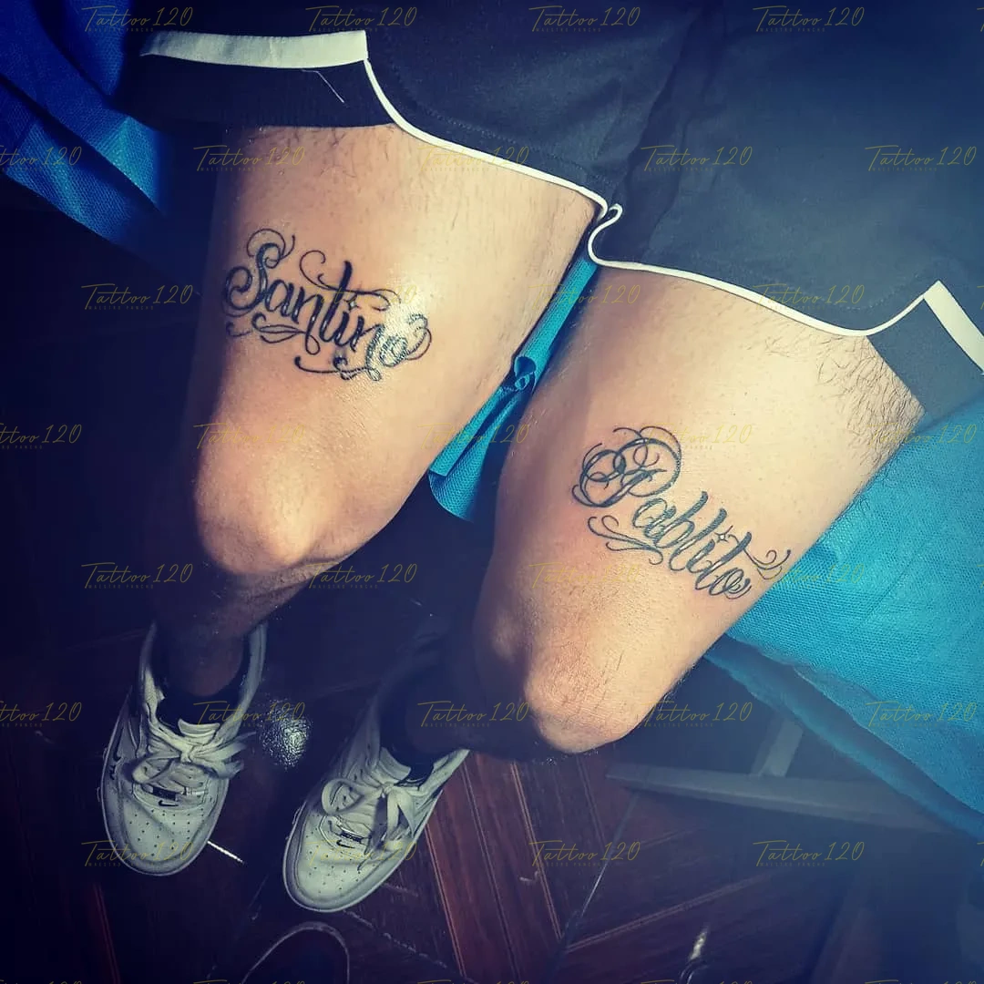 Tatuajes en los muslos de dos personas mostrando los nombres Santino y Pablito en tipografía cursiva fina ornamentada, en estilo de letras, frases y chicano, realizado en el estudio Tattoo120 en Colina, Región Metropolitana.