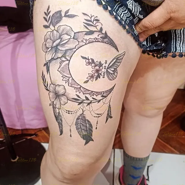 Tatuaje delicado en el muslo de una luna creciente decorada con flores, plumas colgantes y una mariposa con la fecha 05-09-2024, en estilo de línea fina y minimalistas, realizado en el estudio Tattoo120 en Colina, Región Metropolitana.