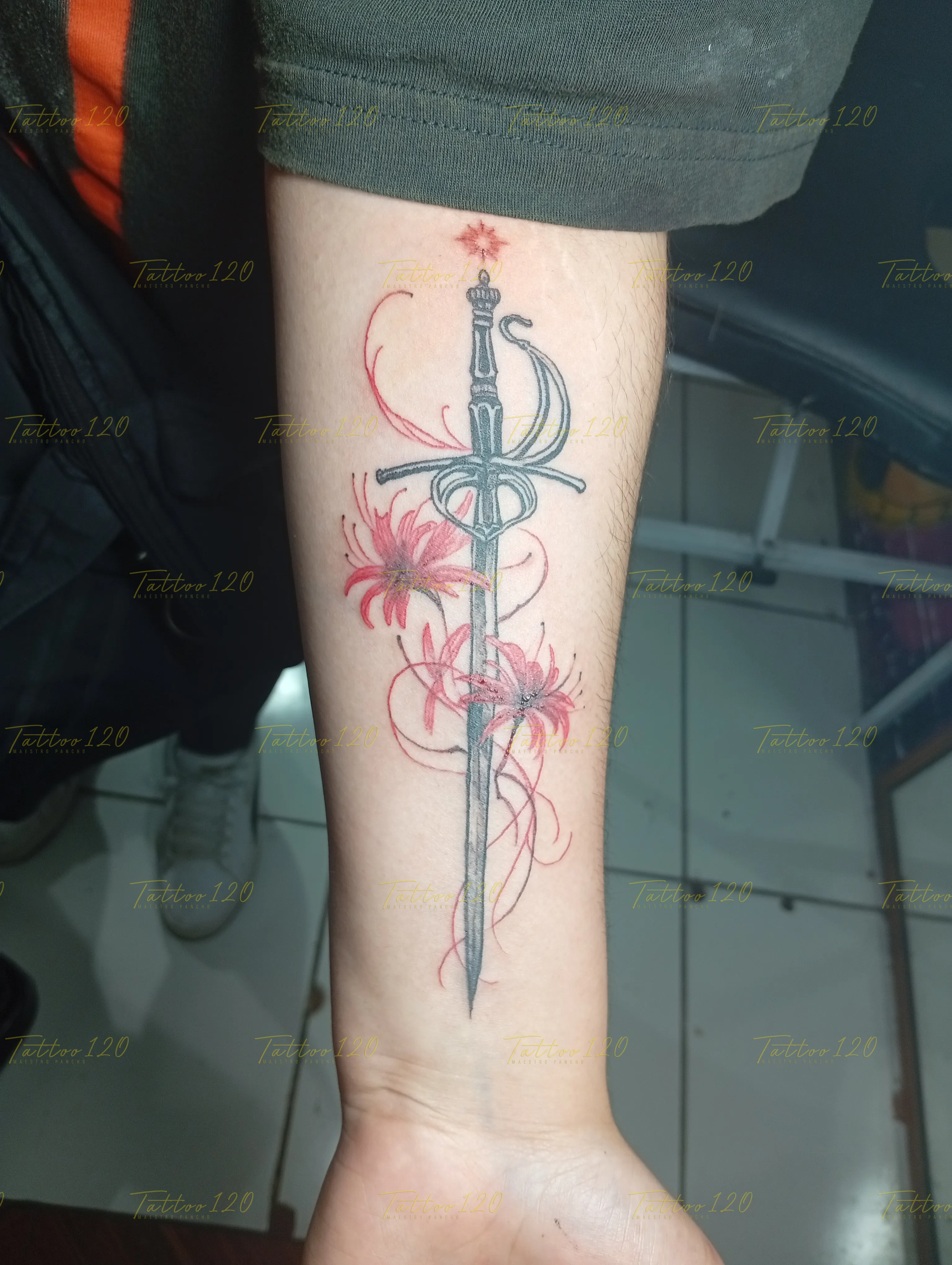 Tatuaje detallado en el antebrazo de una espada estilizada entrelazada con flores de licoris rojas (spider lily), en estilo de línea fina y minimalistas, realizado en el estudio Tattoo120 en Colina, Región Metropolitana.