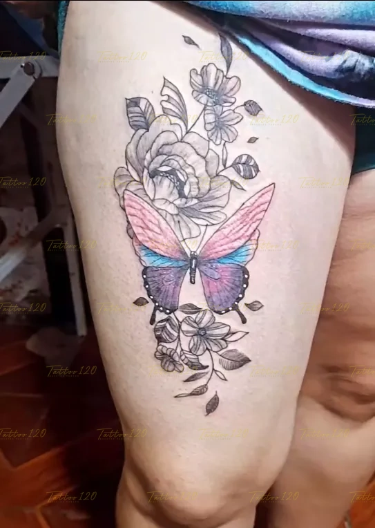 Tatuaje en el muslo de una mariposa con alas en tonos degradados rosa, azul y morado sobre un fondo de flores en tinta negra, en estilo de línea fina y minimalistas, realizado en el estudio Tattoo120 en Colina, Región Metropolitana.