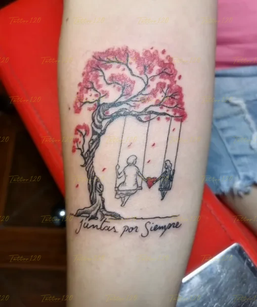 Tatuaje emotivo en el brazo de dos siluetas en un columpio bajo un árbol de hojas rojas con la frase Juntas por Siempre, en estilo de línea fina y minimalistas, realizado en el estudio Tattoo120 en Colina, Región Metropolitana.