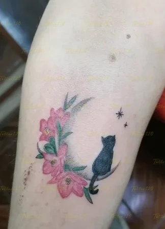 Tatuaje pequeño y delicado de la silueta de un gato negro sentado sobre una luna creciente hecha de flores rosadas y hojitas verdes, en estilo de línea fina y minimalistas, realizado en el estudio Tattoo120 en Colina, Región Metropolitana.