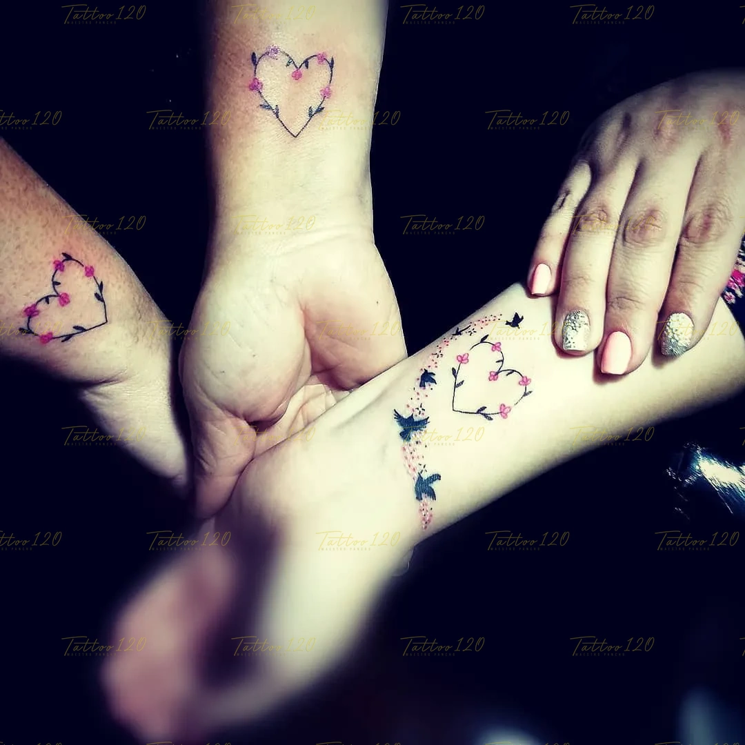 Tatuaje para tres personas en las muñecas con diseños de corazones formados por ramas con pequeñas flores rosadas y siluetas de pájaros, en estilo de línea fina y minimalistas, realizado en el estudio Tattoo120 en Colina, Región Metropolitana.