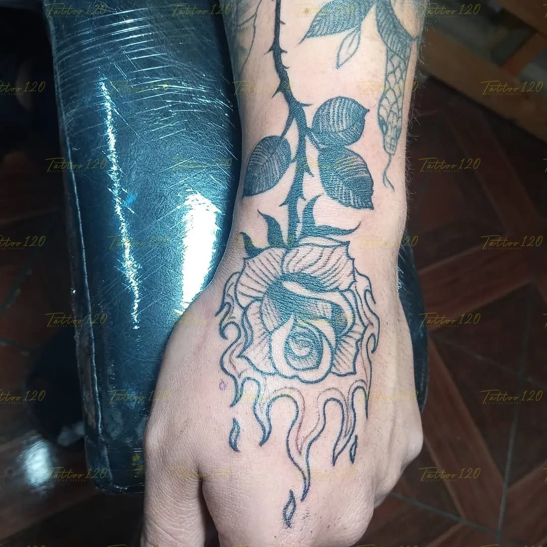 Tatuaje en el dorso de la mano que muestra una rosa con tallo espinoso cuyo contorno inferior simula estarse derritiendo en gotas, en estilo de línea fina y minimalistas, realizado en el estudio Tattoo120 en Colina, Región Metropolitana.