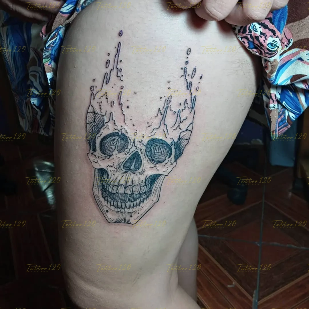 Tatuaje en el muslo de un cráneo humano detallado cuya parte superior se disuelve en ráfagas que simulan fuego o líquido salpicando, en estilo de línea fina y minimalistas, realizado en el estudio Tattoo120 en Colina, Región Metropolitana.