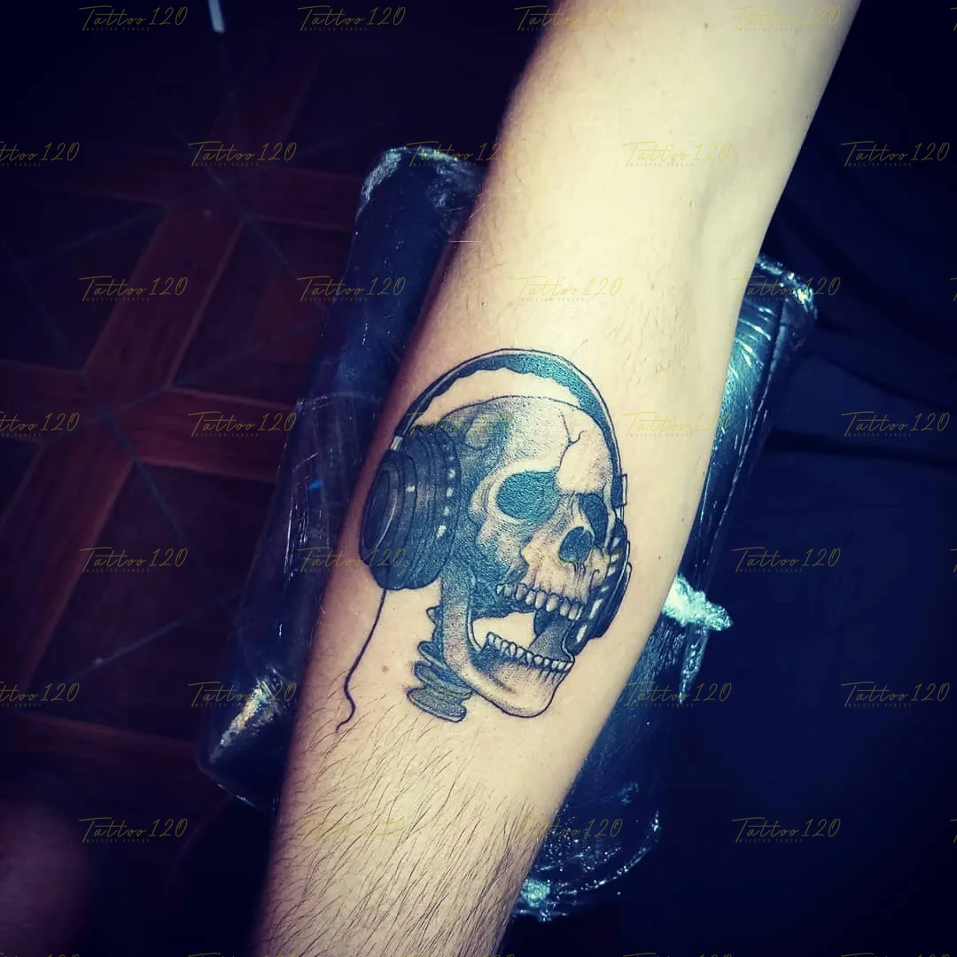 Tatuaje detallado en el antebrazo de una calavera de perfil usando unos audífonos grandes de música con sombreados negros, en estilo de línea fina y minimalistas, realizado en el estudio Tattoo120 en Colina, Región Metropolitana.