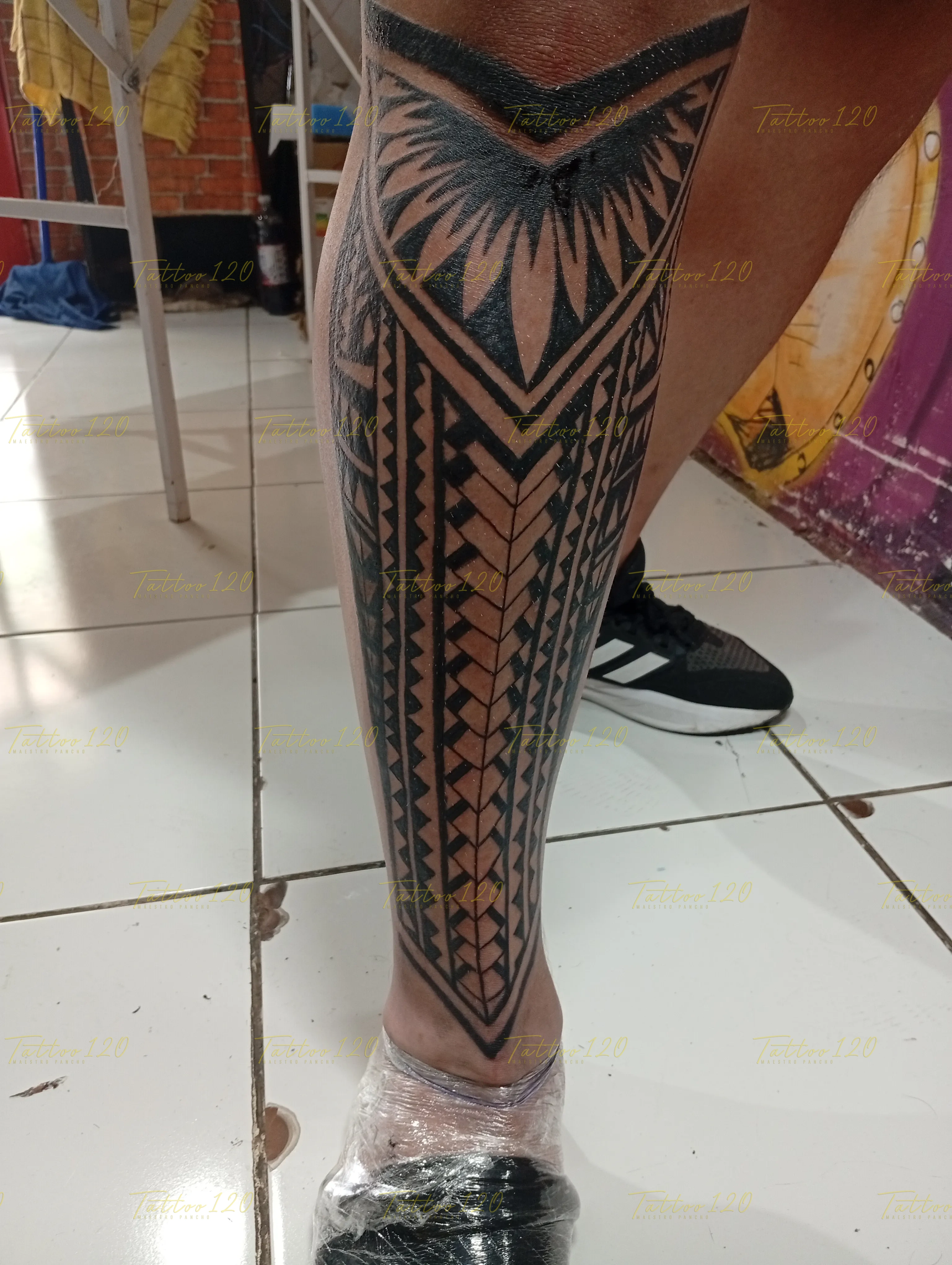 Tatuaje de estilo maorí en toda la pantorrilla con patrones geométricos simétricos de puntas y líneas en tinta negra, en estilo de polinesios y tribales, realizado en el estudio Tattoo120 en Colina, Región Metropolitana.