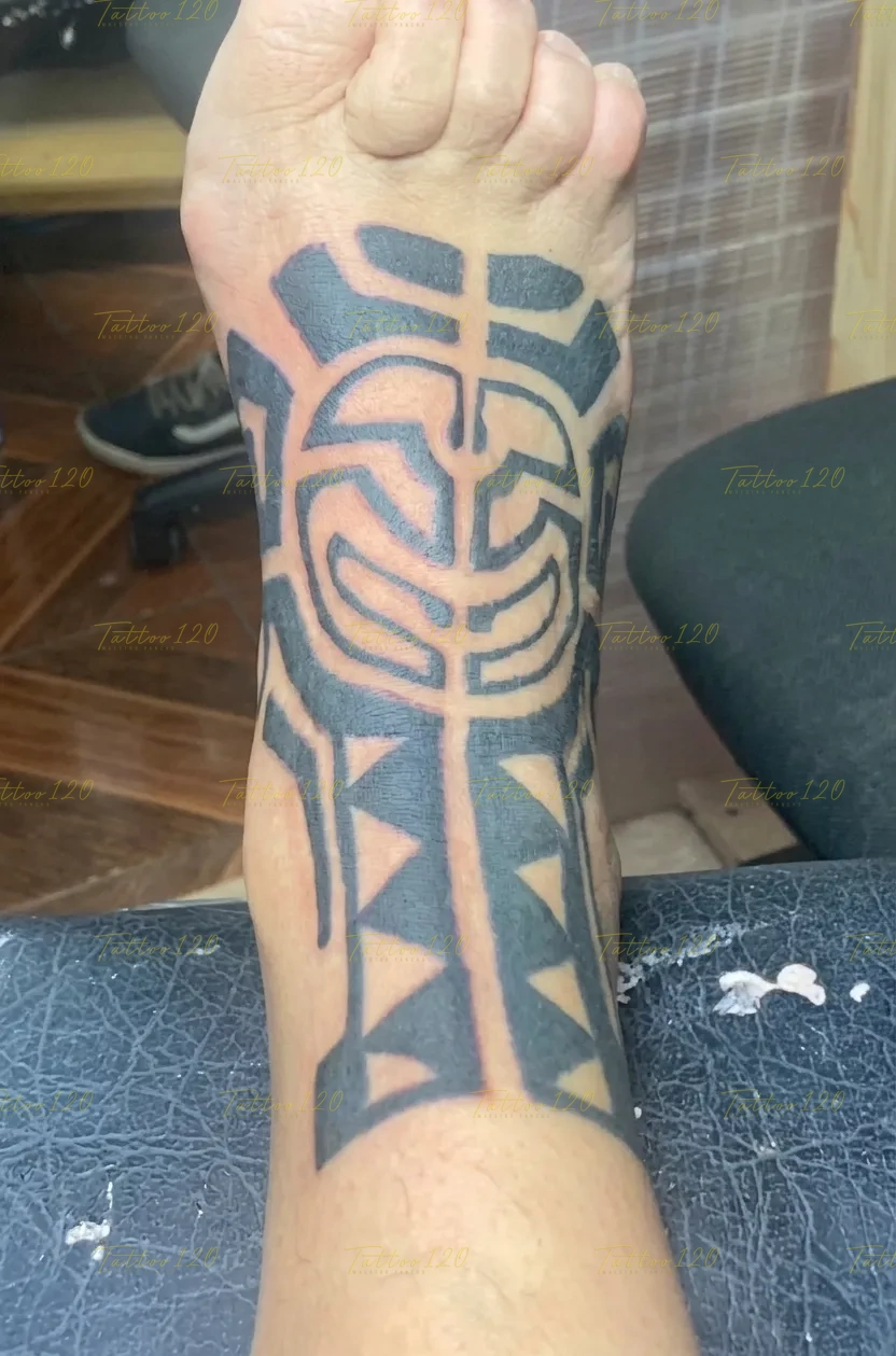 Tatuaje en el empeine del pie con un patrón tribal de líneas curvas gruesas y triángulos en tinta negra sólida, en estilo de polinesios y tribales, realizado en el estudio Tattoo120 en Colina, Región Metropolitana.