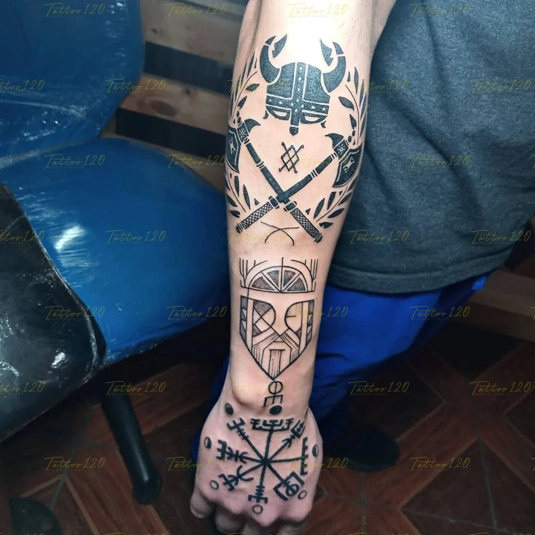 Tatuaje en el antebrazo y mano con simbología nórdica que incluye un casco vikingo, hachas cruzadas y una brújula Vegvísir, en estilo de polinesios y tribales, realizado en el estudio Tattoo120 en Colina, Región Metropolitana.