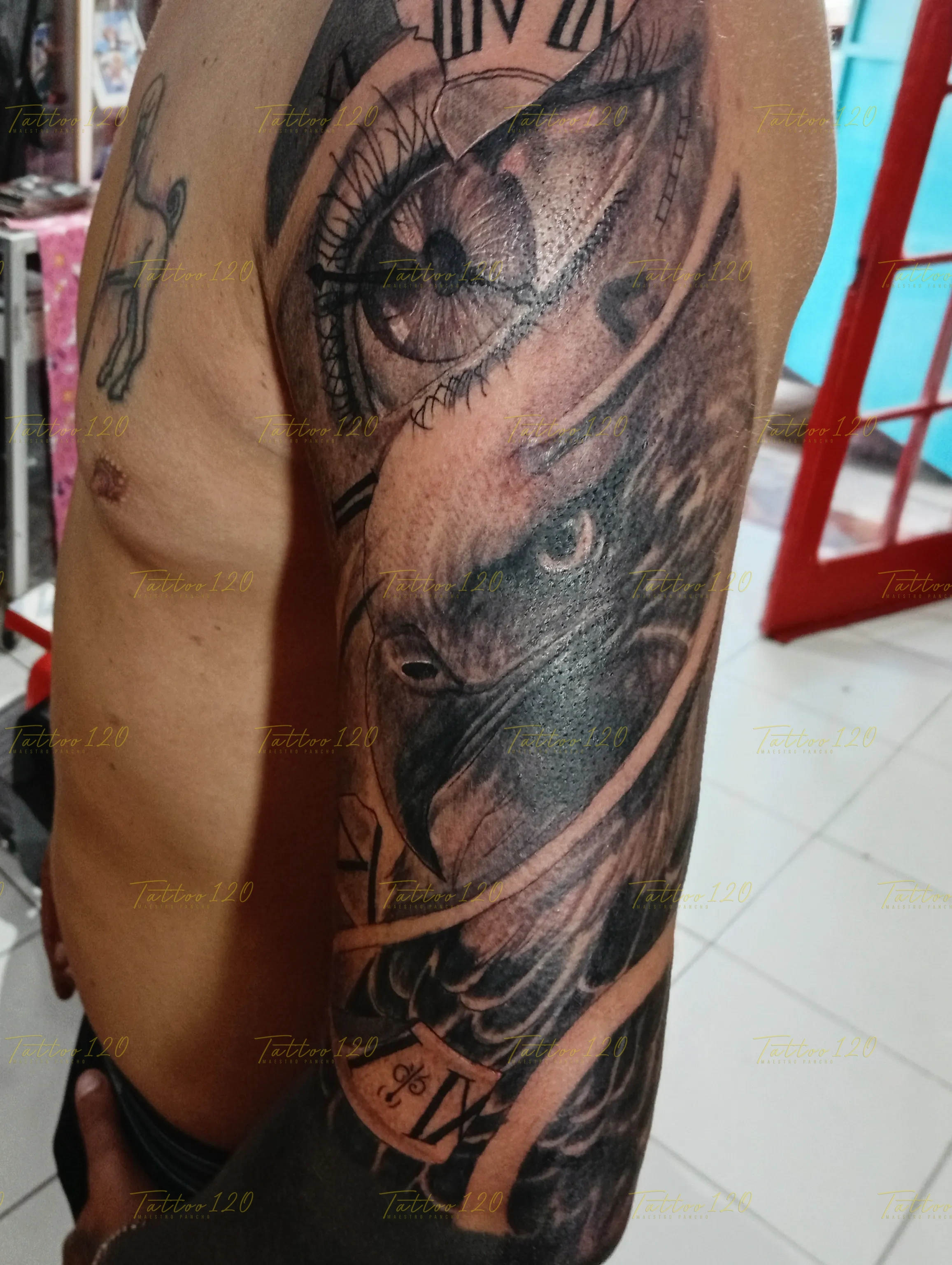 Tatuaje realista en el brazo que combina un primer plano de un ojo, texturas de plumas de águila y números romanos de un reloj, en estilo de realistas, retratos y sombras, realizado en el estudio Tattoo120 en Colina, Región Metropolitana.