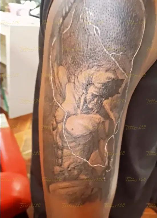 Tatuaje en el brazo de una escultura o figura clásica musculosa rodeada de líneas de rayos brillantes en espacio negativo, en estilo de realistas, retratos y sombras, realizado en el estudio Tattoo120 en Colina, Región Metropolitana.