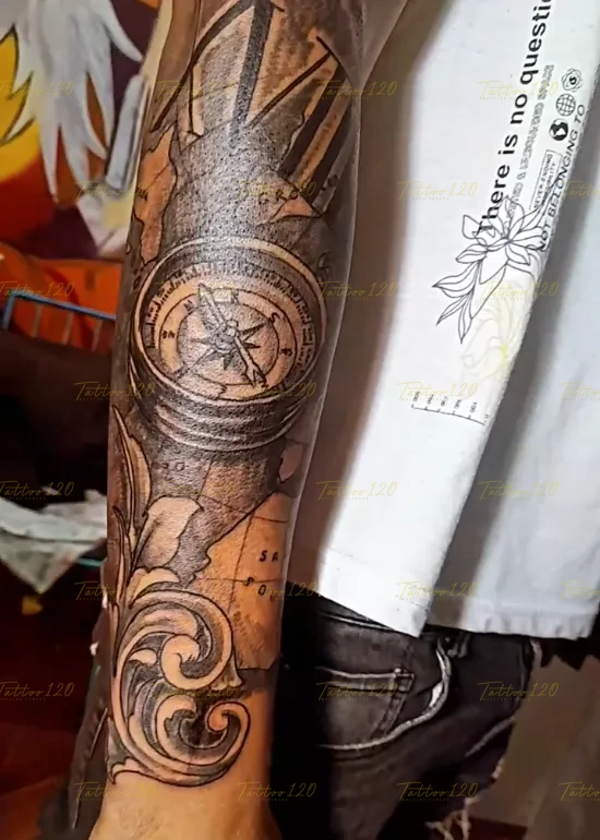 Tatuaje de media manga que integra una brújula detallada sobre un fondo de mapa geográfico antiguo y filigranas, en estilo de realistas, retratos y sombras, realizado en el estudio Tattoo120 en Colina, Región Metropolitana.
