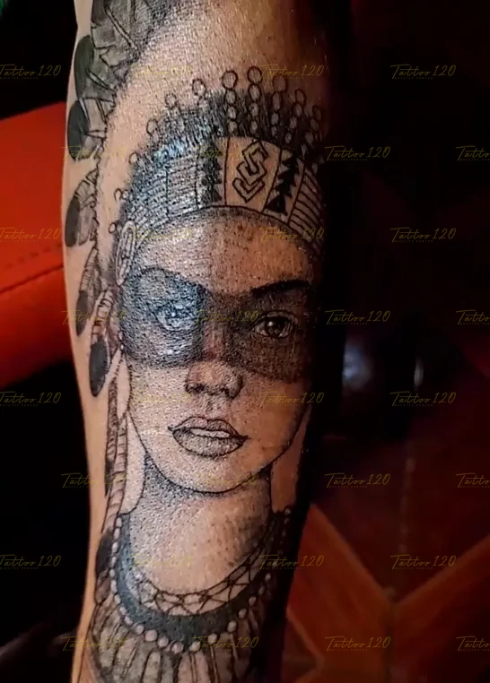 Tatuaje realista en el brazo que retrata el rostro de una mujer nativa americana con pintura de guerra en los ojos y un penacho de plumas detallado, en estilo de realistas, retratos y sombras, realizado en el estudio Tattoo120 en Colina, Región Metropolitana.