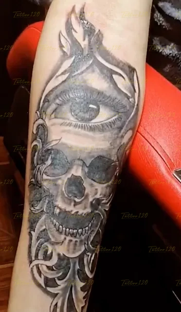 Tatuaje en el antebrazo que integra un ojo místico sobre un cráneo humano detallado con ornamentos fluidos, en estilo de realistas, retratos y sombras, realizado en el estudio Tattoo120 en Colina, Región Metropolitana.