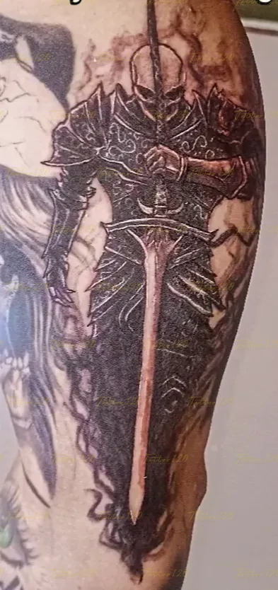 Tatuaje realista en el brazo de un guerrero con armadura oscura ornamentada sosteniendo una gran espada vertical, en estilo de realistas, retratos y sombras, realizado en el estudio Tattoo120 en Colina, Región Metropolitana.