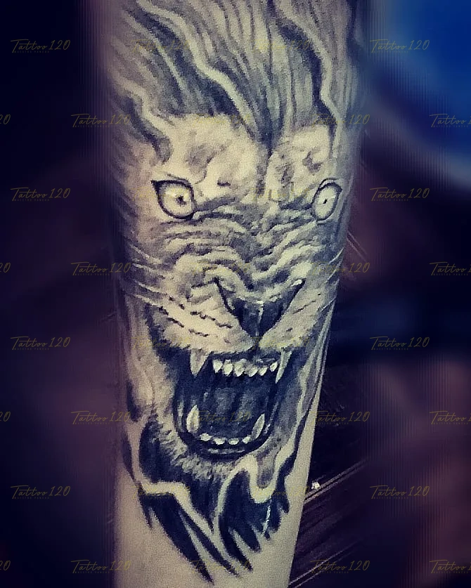 Tatuaje realista en el brazo que muestra un primer plano del rostro de un león rugiendo con colmillos expuestos y melena difuminada, en estilo de realistas, retratos y sombras, realizado en el estudio Tattoo120 en Colina, Región Metropolitana.