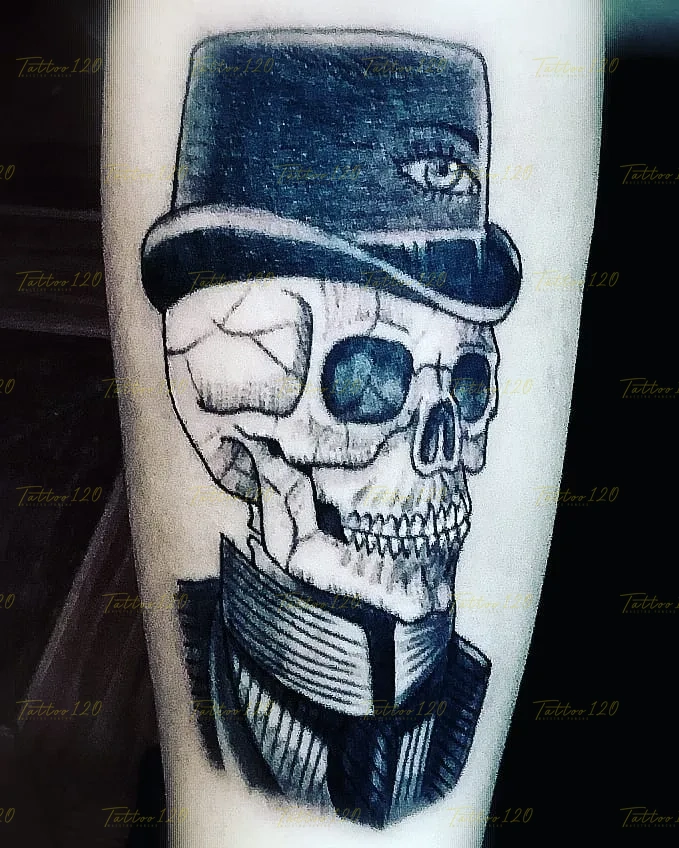 Tatuaje en blanco y gris de una calavera vestida con traje formal y un sombrero de copa alta decorado con un ojo místico, en estilo de realistas, retratos y sombras, realizado en el estudio Tattoo120 en Colina, Región Metropolitana.