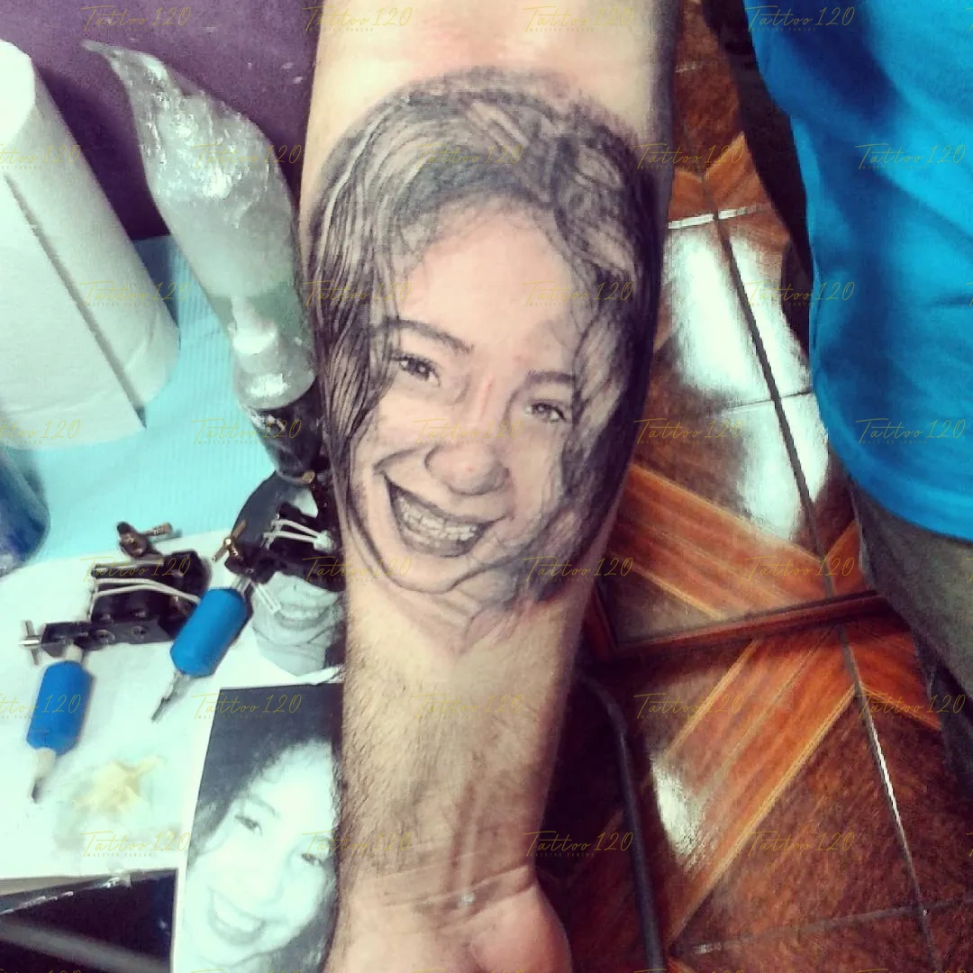 Tatuaje de retrato realista en el antebrazo de una niña sonriente mostrando sus brackets, basado en una fotografía de referencia inferior, en estilo de realistas, retratos y sombras, realizado en el estudio Tattoo120 en Colina, Región Metropolitana.