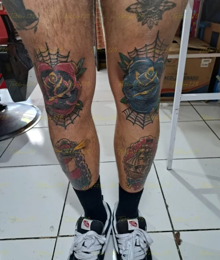 Tatuaje en ambas rodillas que muestra una rosa roja y una rosa azul enmarcadas por fondos de telarañas tradicionales con un faro y un barco abajo, en estilo de tradicional y neo tradicional, realizado en el estudio Tattoo120 en Colina, Región Metropolitana.