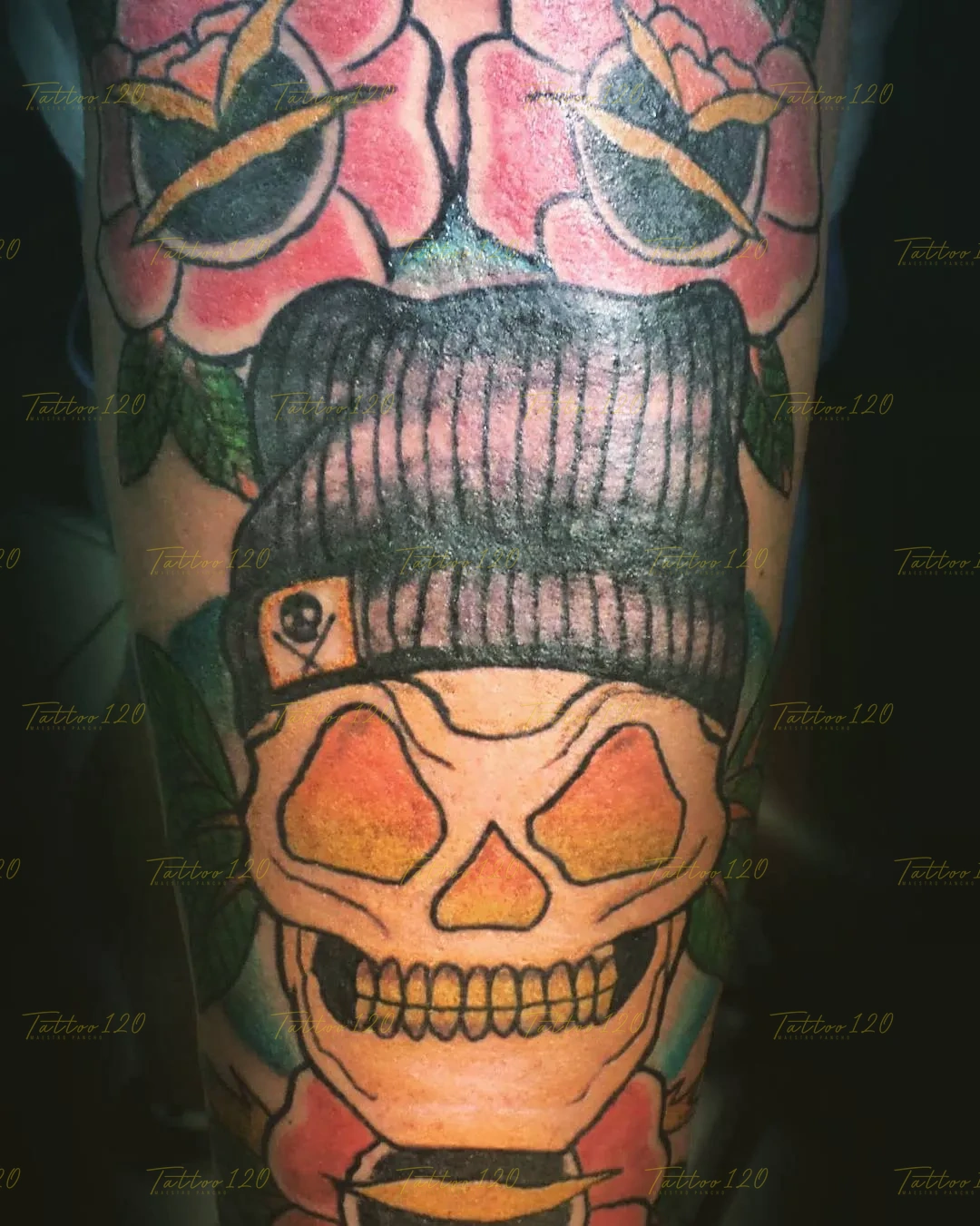 Tatuaje a color de un cráneo con cuencas amarillas usando un gorro de lana con parche de pirata, rodeado de rosas rojas tradicionales, en estilo de tradicional y neo tradicional, realizado en el estudio Tattoo120 en Colina, Región Metropolitana.